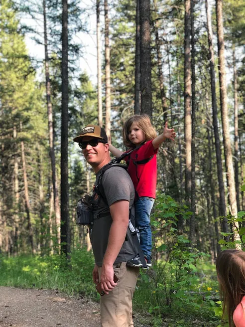 Josh carrying the youngest on his shoulders down a forest trail, the child pointing ahead