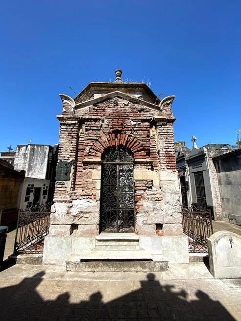A square stone mausoleum with a dark iron door and a white cross, classical architecture in the cemetery