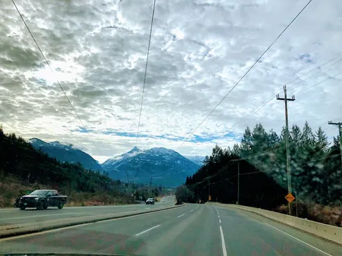The Sea to Sky highway seen through the windscreen, snow topped peaks ahead under heavy cloud