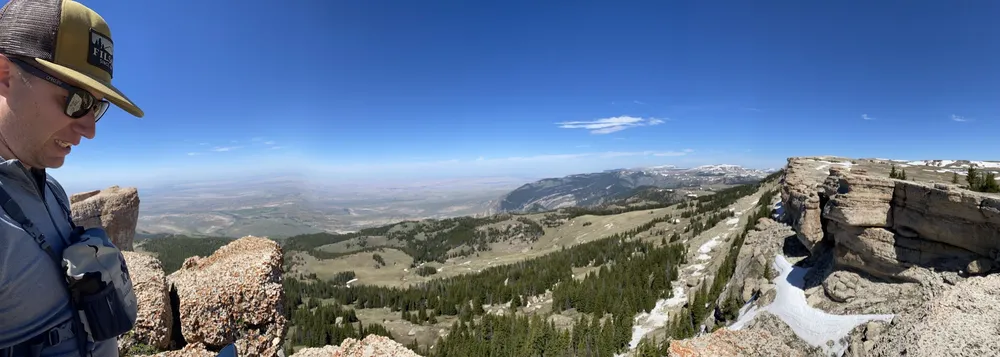 Josh at the left of a wide panorama from the top of the Big Horns, alpine meadows and snow patches falling away to the basin