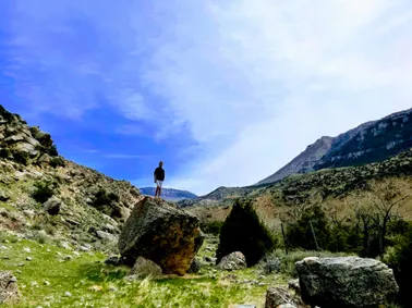 Preston standing on top of a huge lone boulder in a green valley, the Big Horn escarpment behind him