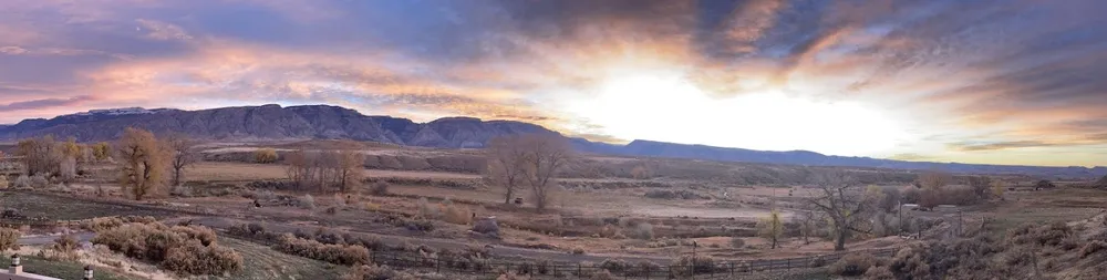 A wide sunrise over the ranch, the Big Horn escarpment along the horizon and bare cottonwoods across the flat