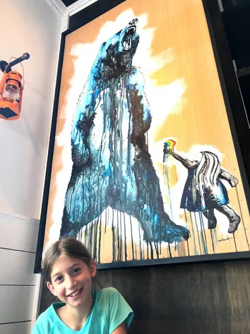 One of the girls grinning beneath a large painting of a bear being offered an ice cream
