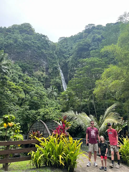 Josh and two of the boys on a path of tropical planting, a tall waterfall dropping down the green cliff behind