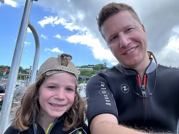 Josh and Case in wetsuits on the boat before a dive, both grinning at the camera