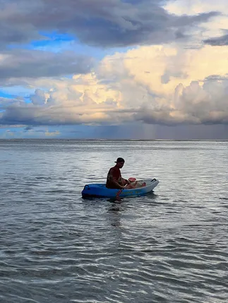 Josh sitting on a kayak in the shallows at dusk with one of the children, heavy cloud out over the reef