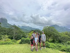 All six of them on a grassy lookout on Moorea, jagged green peaks and low cloud filling the view behind