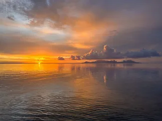 A wide orange sunset over the lagoon, Moorea low on the horizon and the whole sky mirrored in the water
