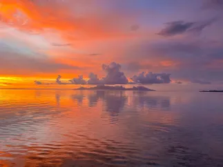 Pink and orange cloud filling the sky above Moorea, the colour repeated exactly in the still lagoon