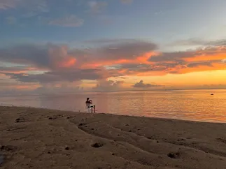 Josh alone in a white chair at the tide line, looking out at the sunset across the lagoon