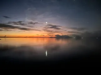 The last of the light over the lagoon after sunset, a bright planet above the cloud and its reflection on the water