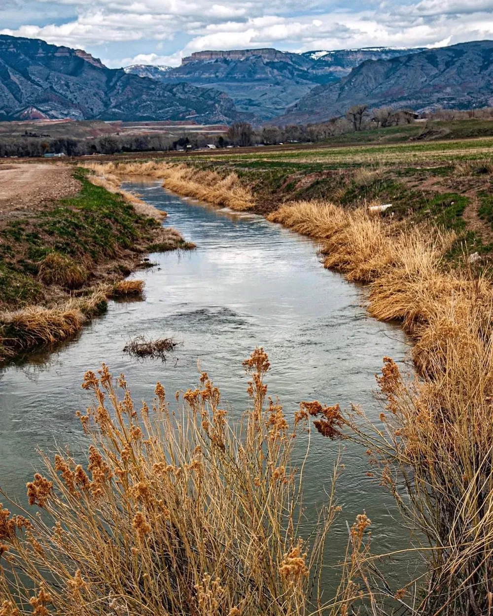 The creek running full between banks of dry autumn grass, the layered face of the Big Horns under heavy cloud behind