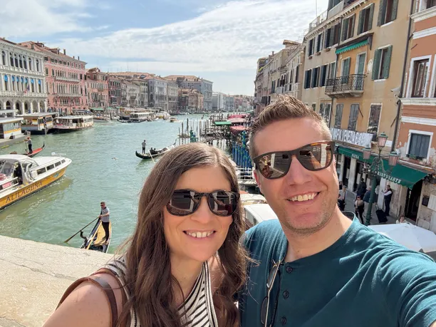 Emily and Josh on the Rialto bridge, the Grand Canal lined with palazzi and gondolas stretching away behind them