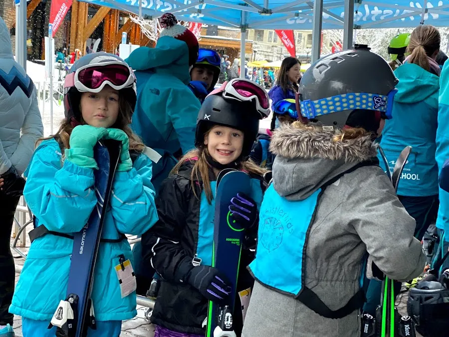 Three of the children in helmets and goggles holding their skis at the Whistler ski school tent