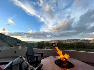A notebook on a lap beside a lit fire pit on the patio, the valley and escarpment beyond at sunset
