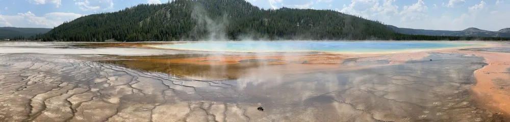 The Grand Prismatic Spring, steam lifting off the blue centre with orange bacterial mats running out across the flats