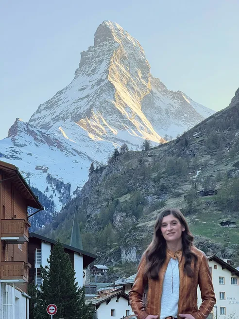 Emily in a tan leather jacket on a Zermatt street, the Matterhorn rising above the chalets with its face lit gold